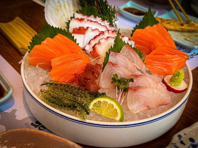 Mỗi lát sashimi mỏng, tinh tế như một tác phẩm nghệ thuật, tận dụng vị ngon đặc trưng của cá hồi, tôm và hải sản khác để tạo nên một trải nghiệm ẩm thực đầy tươi ngon. Món sashimi là một hành trình thưởng thức hương vị tinh tế và sự tươi mới của đại dương